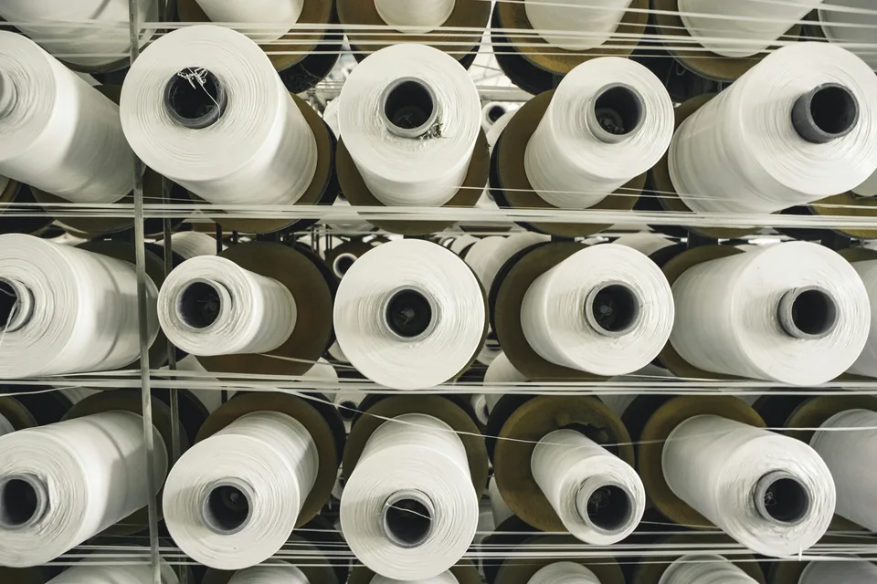 Rows of white yarn or filament spools feeding fine strands across a production rack.