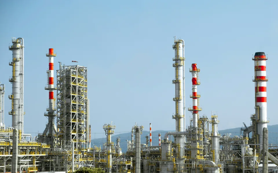 Tall process columns, yellow access platforms and pipework under a clear blue sky.