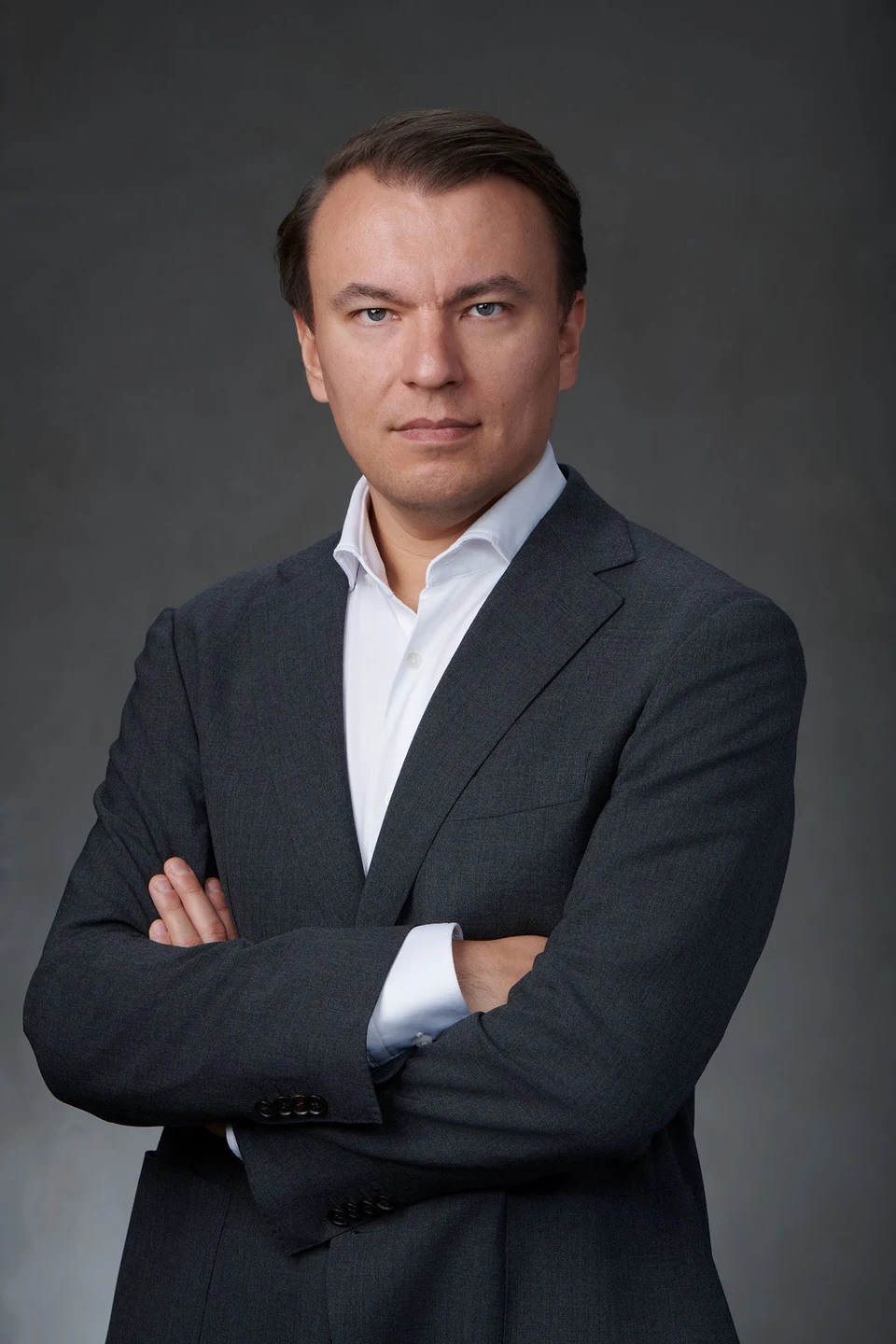 Stan Sabitovs in a dark suit and white shirt, standing with his arms crossed.