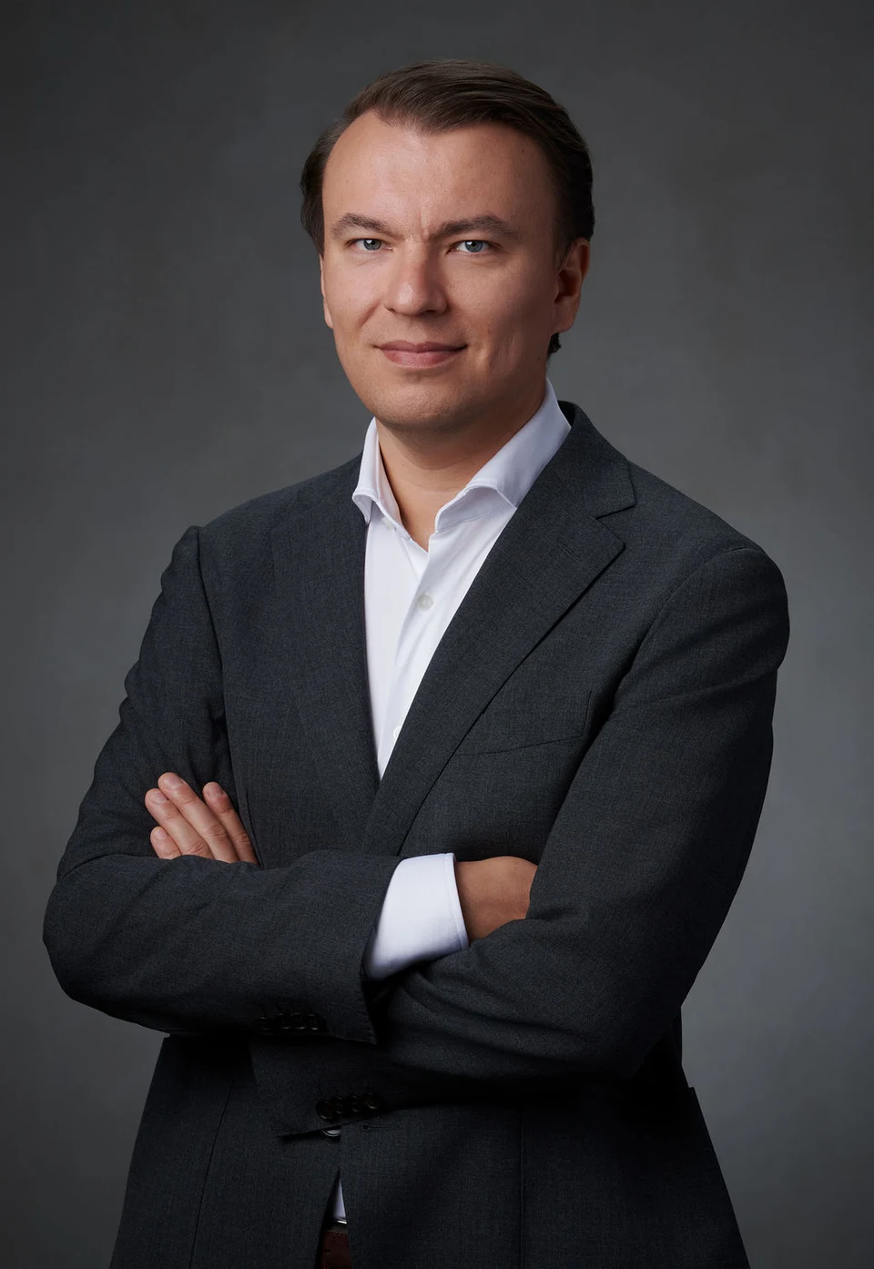 Stan Sabitovs in a dark suit and white shirt, with a slight smile and arms crossed.