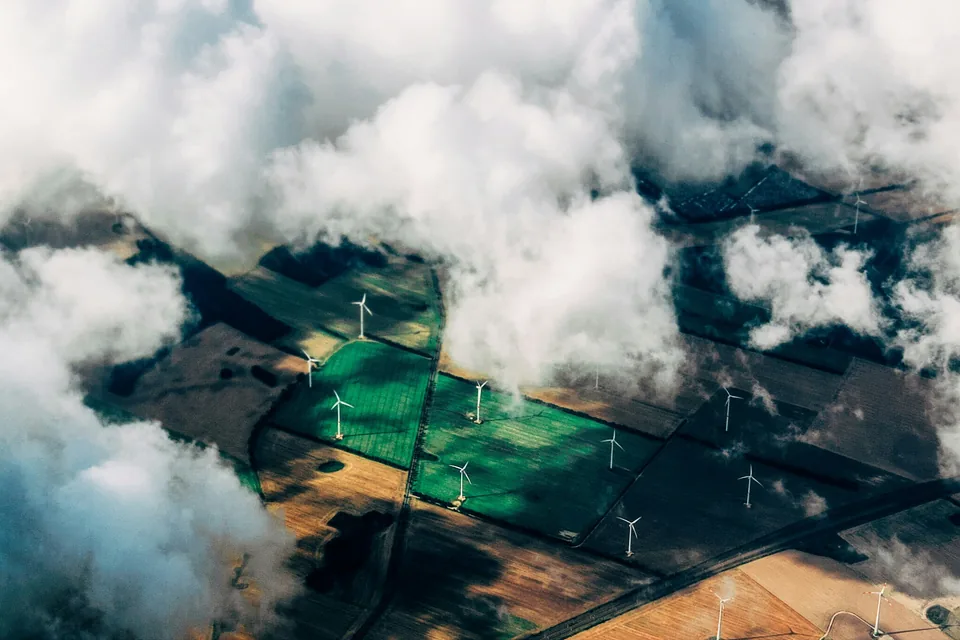 Aerial view of wind turbines across agricultural fields, partly framed by clouds.