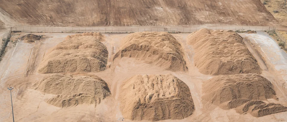 Large segregated piles of wood chips on a paved industrial stockyard.