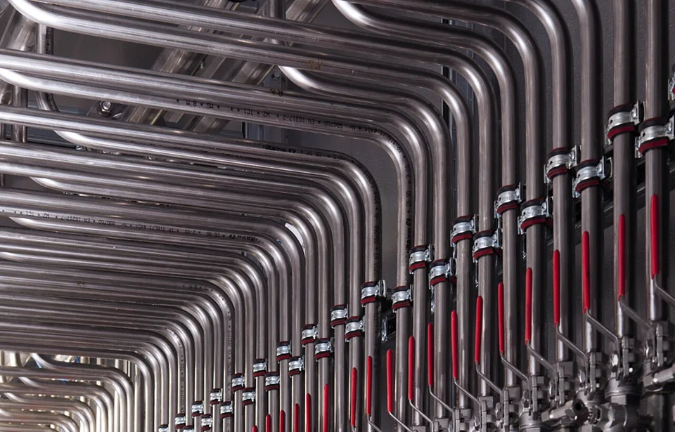 Parallel stainless-steel pipes and red valve handles in biogas-upgrading equipment.