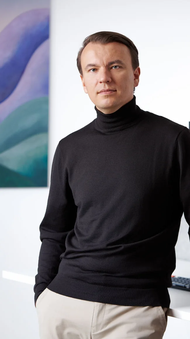 Stan Sabitovs in a dark turtleneck, leaning beside an office desk.