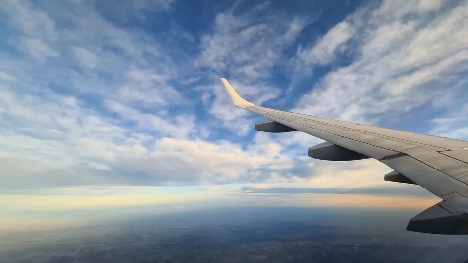 An unbranded aircraft wing above clouds in the morning sky, illustrating aviation as an end use for fuel.